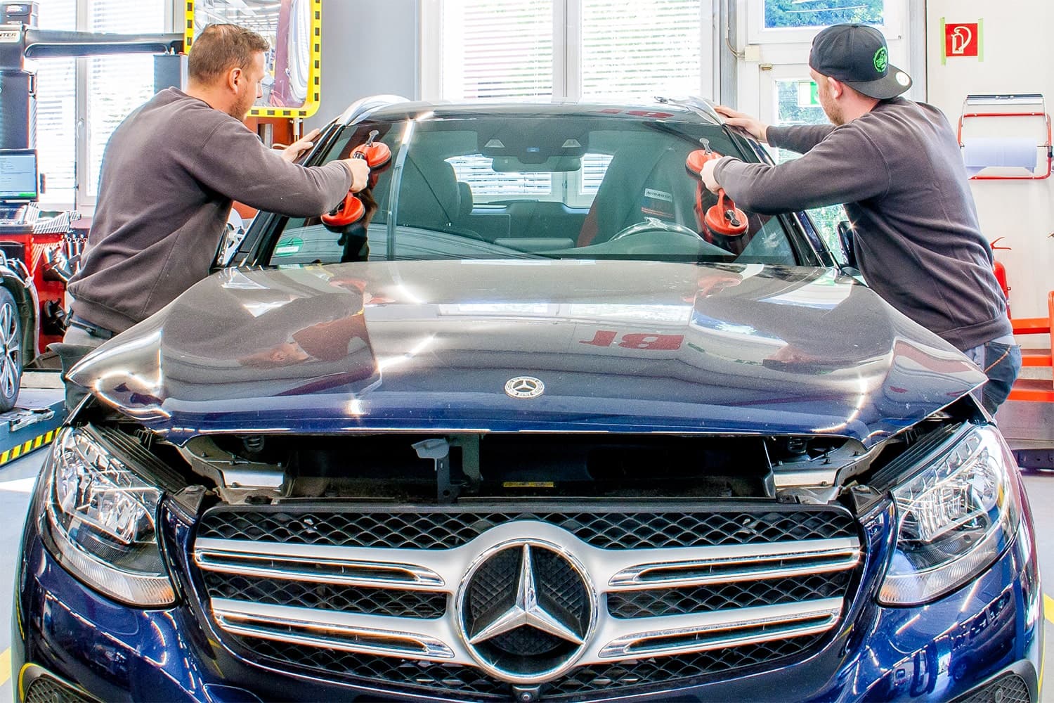 Zwei Mitarbeiter setzen mit Saughebern eine neue Windschutzscheibe in ein Fahrzeug ein